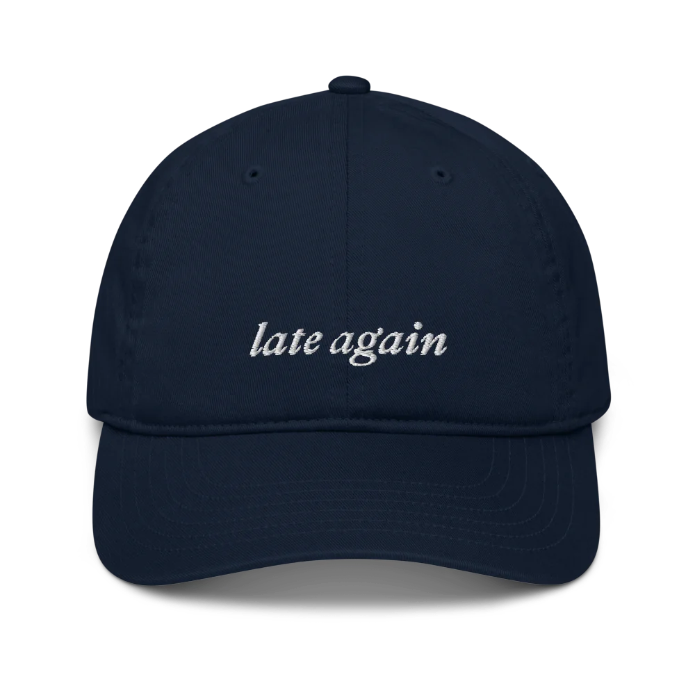 Navy baseball hat with 'late again' text embroidered in white on a white background