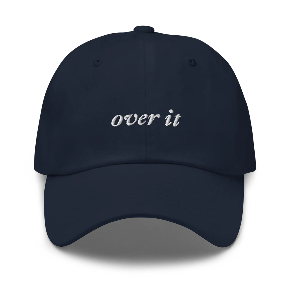 Navy blue baseball hat with 'over it' text embroidered in white on a white background