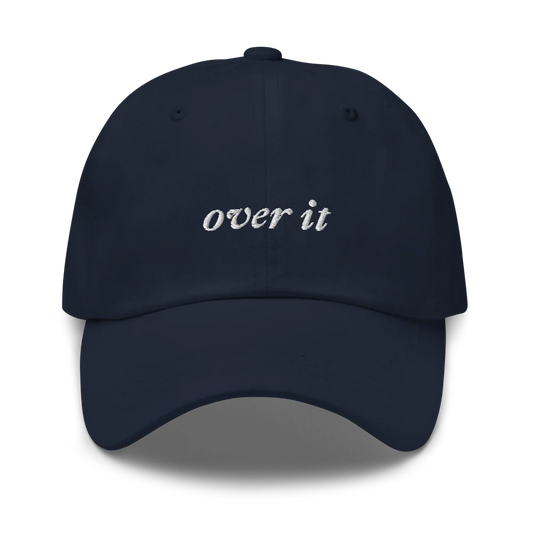 Navy blue baseball hat with 'over it' text embroidered in white on a white background
