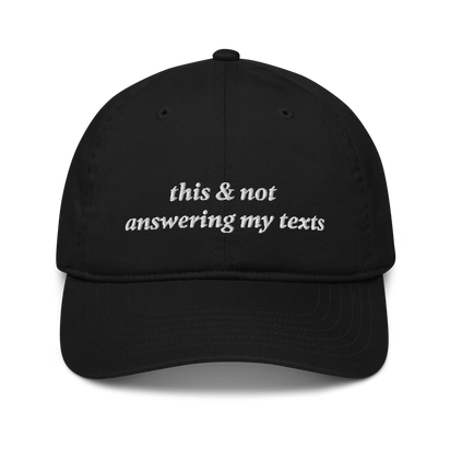 Black baseball hat with white text 'this & not answering my texts' on a white background