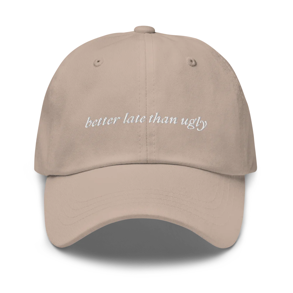 beige baseball hat with 'better late than ugly' text embroidered in white on a white background