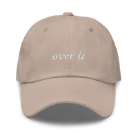 beige baseball hat with 'over it' text embroidered in white on a white background