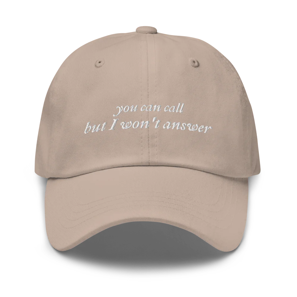 Beige baseball hat with white embroidered text 'you can call but I won't answer' on a white background