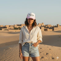 Person wearing a white shirt, denim shorts, and a pink cap with text saying "better late than ugly"  in a desert setting.