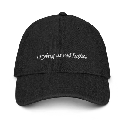 black denim baseball hat with 'crying at red lights' text embroidered in white on a white background