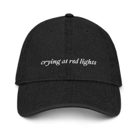 black denim baseball hat with 'crying at red lights' text embroidered in white on a white background