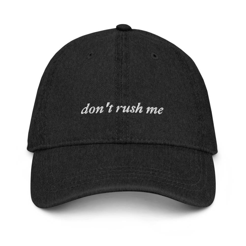 Black denim baseball hat with 'don't rush me' text embroidered in white on a white background
