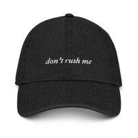 Black denim baseball hat with 'don't rush me' text embroidered in white on a white background
