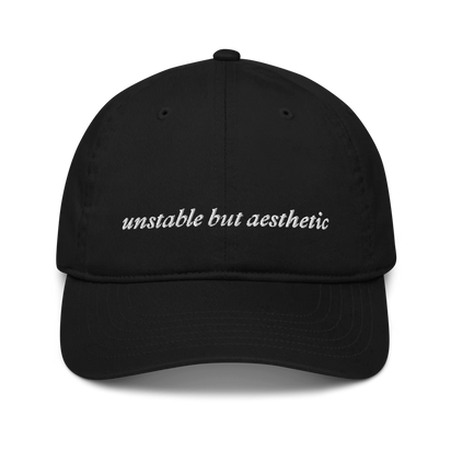 Black baseball hat with 'unstable but aesthetic' text embroidered in white on a white background