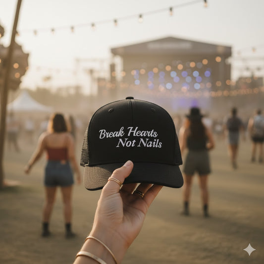 Black cap with 'Break Hearts Not Nails' text held in front of a blurred concert scene