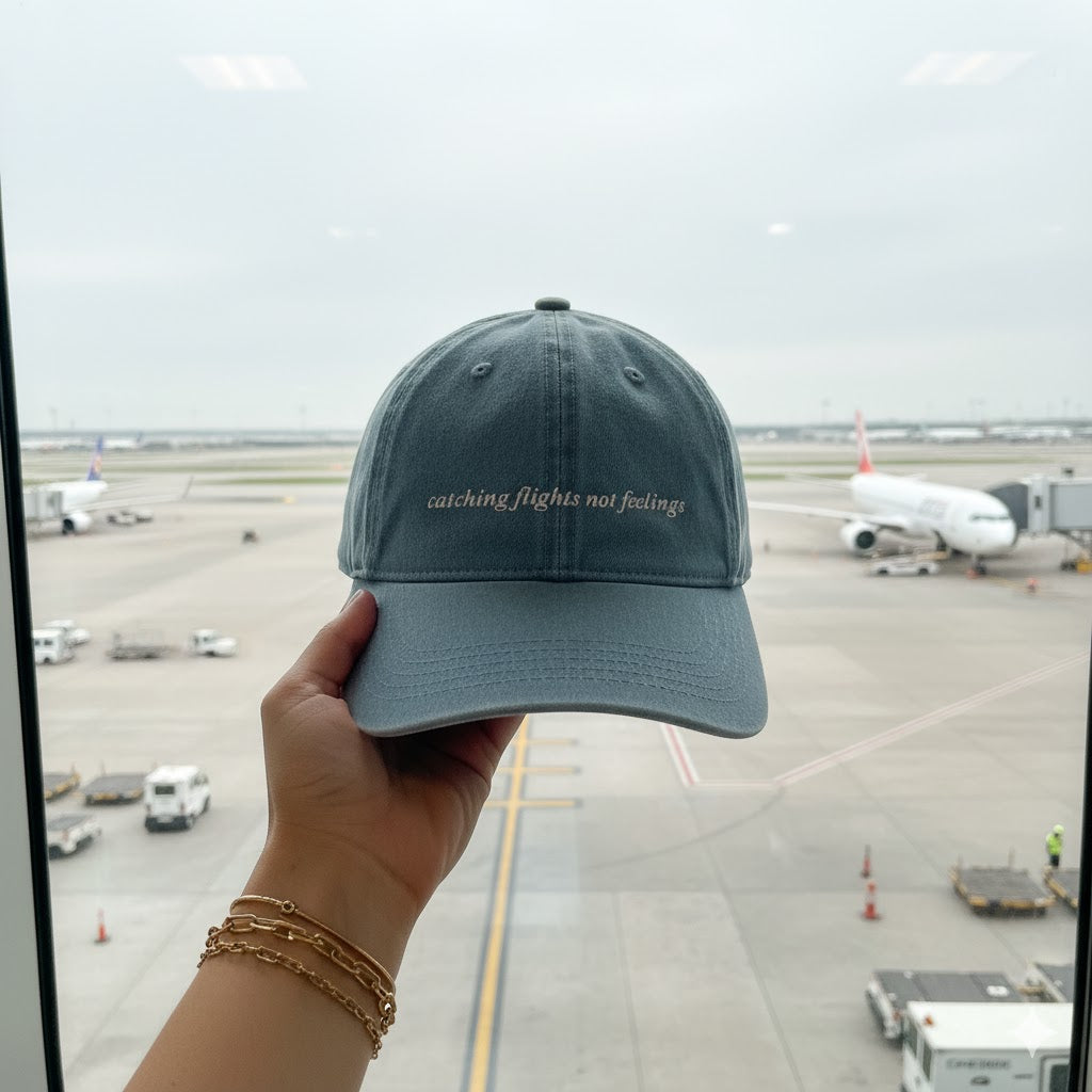 Person holding a cap with 'catching flights not feelings' text at an airport.