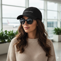 Woman wearing Black denim baseball hat with 'catching flights not feelings' text embroidered in white on a white background