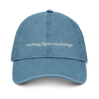  denim baseball hat with 'catching flights not feelings' text embroidered in white on a white background