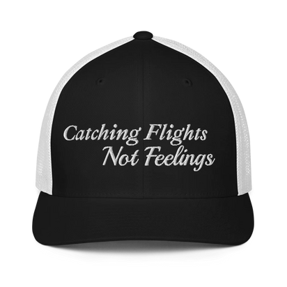 Black and white trucker hat with 'Catching Flights Not Feelings' text embroideredin white  on a white background