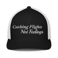 Black and white trucker hat with 'Catching Flights Not Feelings' text embroideredin white  on a white background