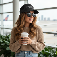 woman wearing Black trucker hat with 'Catching Flights Not Feelings' text embroideredin white  on a white background