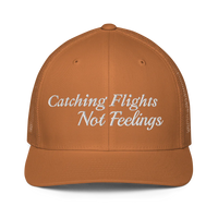 brown trucker hat with 'Catching Flights Not Feelings' text embroideredin white  on a white background
