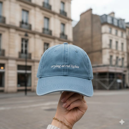 Light blue cap with 'crying at red lights' text held in front of a city street background