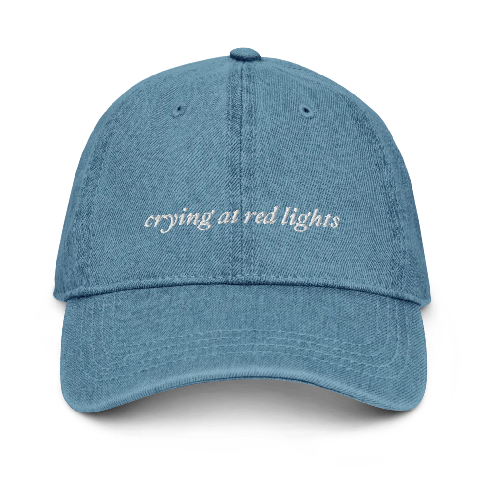 denim baseball hat with 'crying at red lights' text embroidered in white on a white background