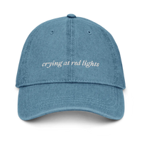 denim baseball hat with 'crying at red lights' text embroidered in white on a white background