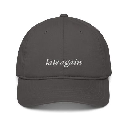Gray baseball hat with 'late again' text embroidered in white on a white background