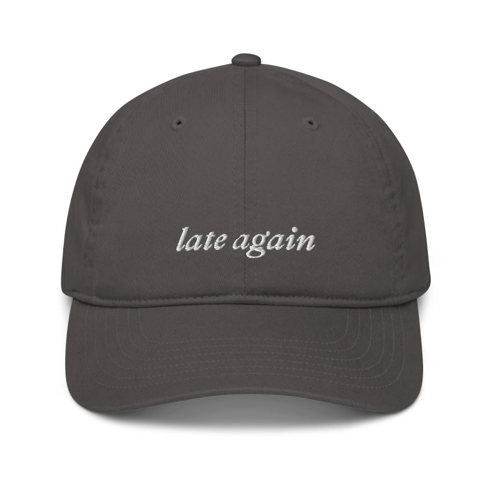 Gray baseball hat with 'late again' text embroidered in white on a white background