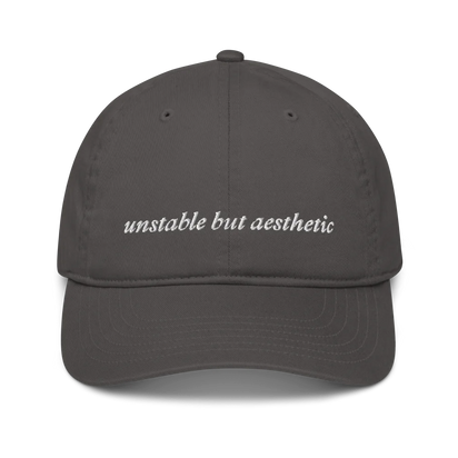 Gray baseball hat with 'unstable but aesthetic' text embroidered in white on a white background