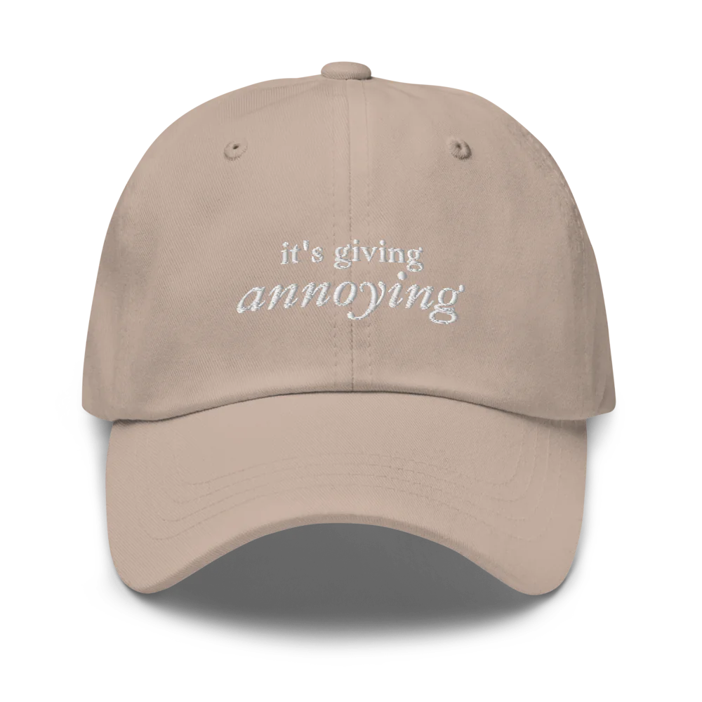 Beige baseball hat with white text 'it's giving annoying' embroidered on front