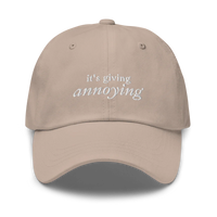 Beige baseball hat with white text 'it's giving annoying' embroidered on front