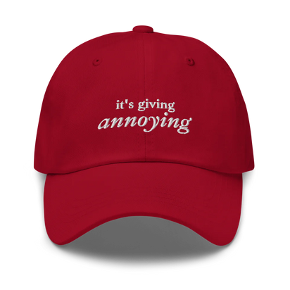 Red baseball hat with white text 'it's giving annoying' embroidered on front