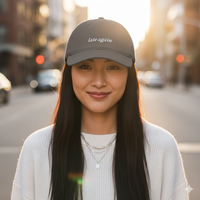 Woman wearing a cap with 'late again' text on a city street.