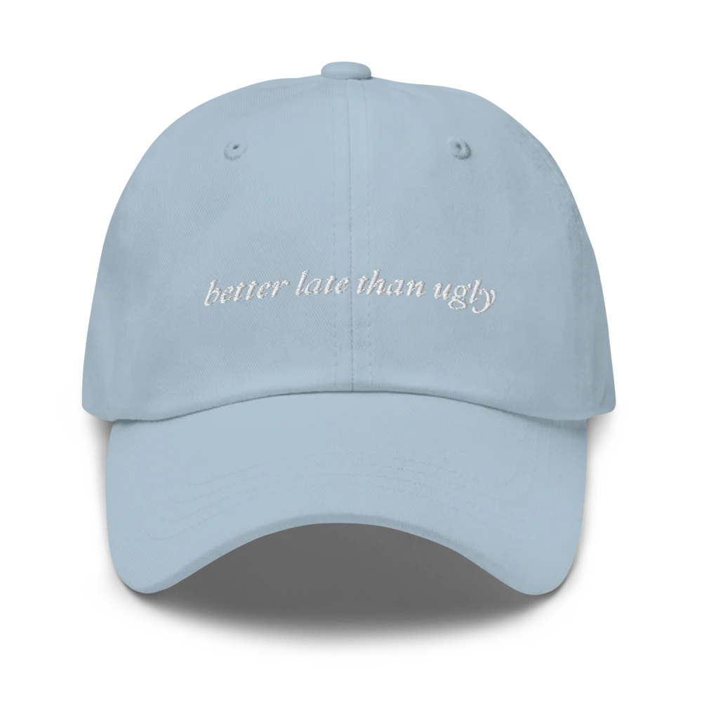 light blue baseball hat with 'better late than ugly' text embroidered in white on a white background