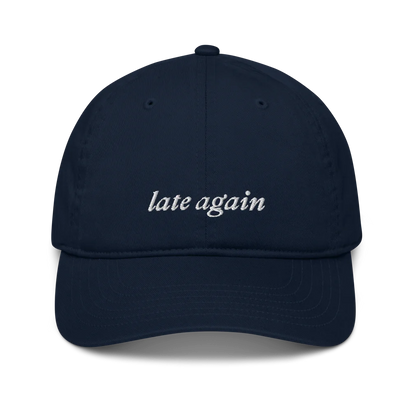 Navy baseball hat with 'late again' text embroidered in white on a white background