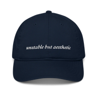 Navy blue baseball hat with 'unstable but aesthetic' text embroidered in white on a white background