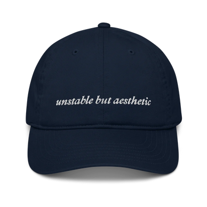 Navy blue baseball hat with 'unstable but aesthetic' text embroidered in white on a white background