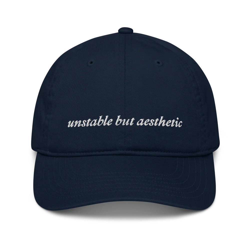 Navy blue baseball hat with 'unstable but aesthetic' text embroidered in white on a white background