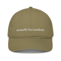 Olive green baseball hat with 'unstable but aesthetic' text embroidered in white on a white background