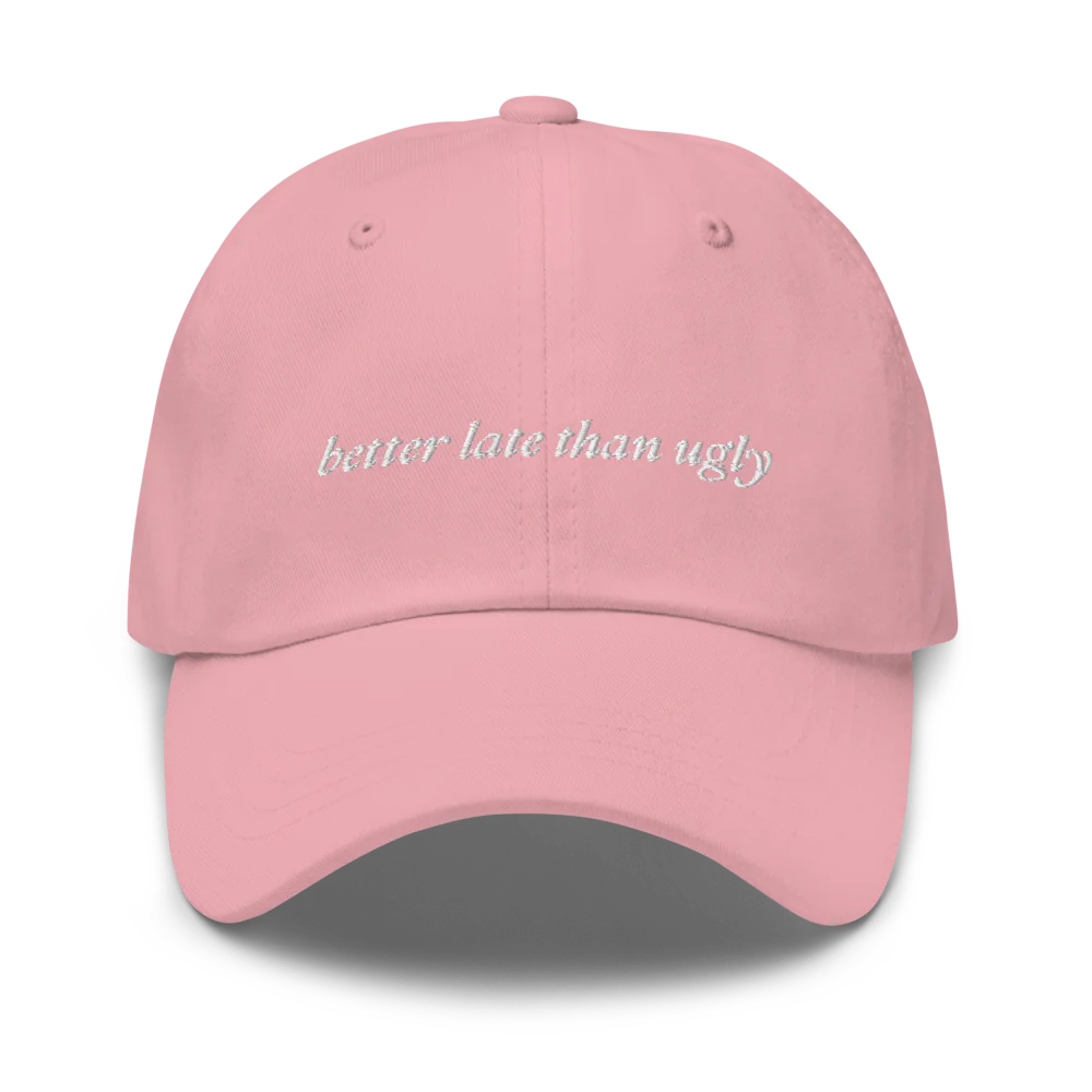 pink baseball hat with 'better late than ugly' text embroidered in white on a white background