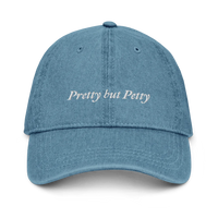 Denim baseball hat with 'Pretty but Petty' text embroidered in white on a white background