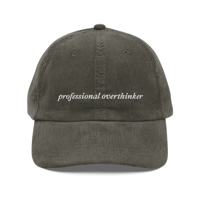 green corduroy baseball hat with 'professional overthinker' text embroidered in white on a white background