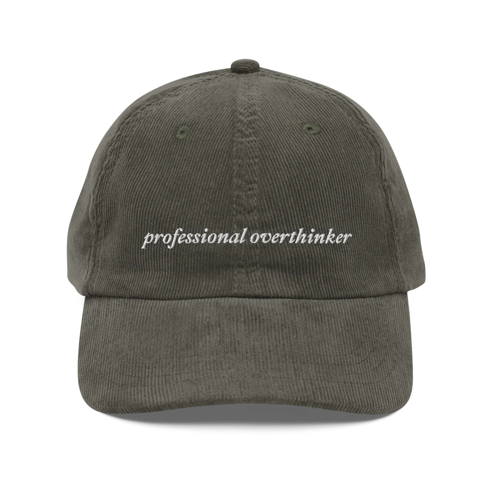 green corduroy baseball hat with 'professional overthinker' text embroidered in white on a white background
