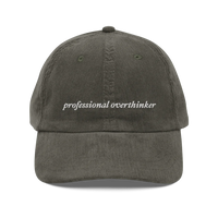 green corduroy baseball hat with 'professional overthinker' text embroidered in white on a white background