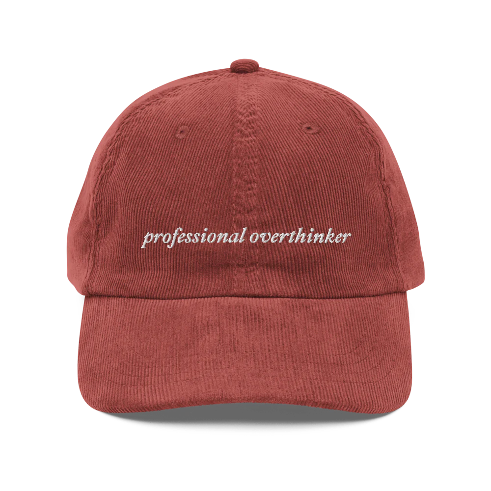 red corduroy baseball hat with 'professional overthinker' text embroidered in white on a white background