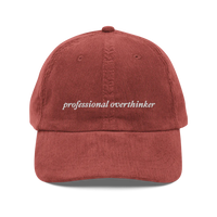 red corduroy baseball hat with 'professional overthinker' text embroidered in white on a white background