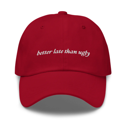 Red baseball hat with 'better late than ugly' text embroidered in white on a white background