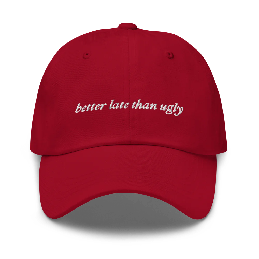 Red baseball hat with 'better late than ugly' text embroidered in white on a white background