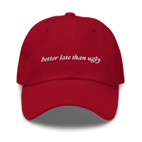 Red baseball hat with 'better late than ugly' text embroidered in white on a white background