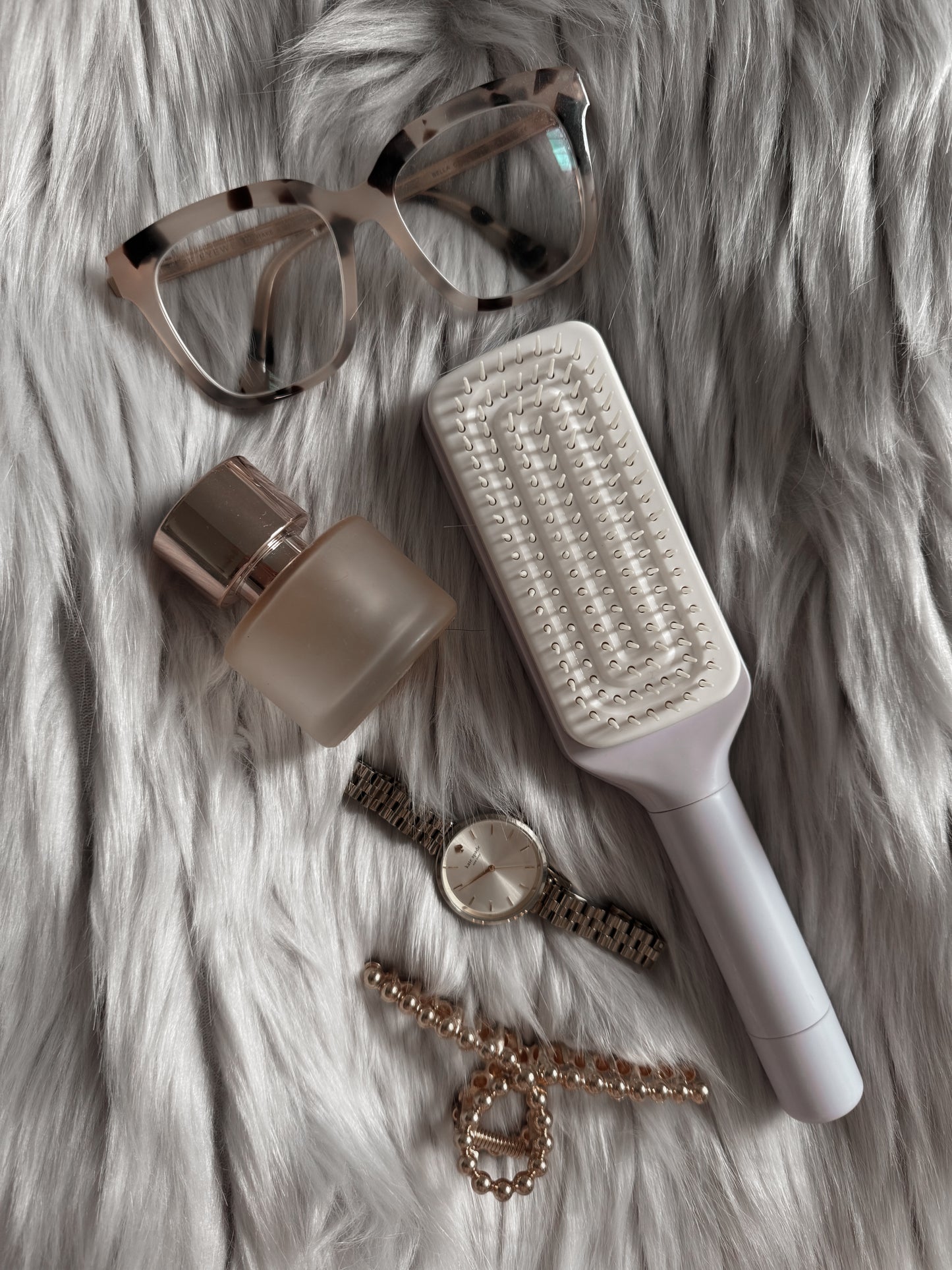 purple self cleaning hairbrush, sunglasses, bottle, watch, and bracelet on a fur surface