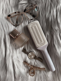 purple self cleaning hairbrush, sunglasses, bottle, watch, and bracelet on a fur surface