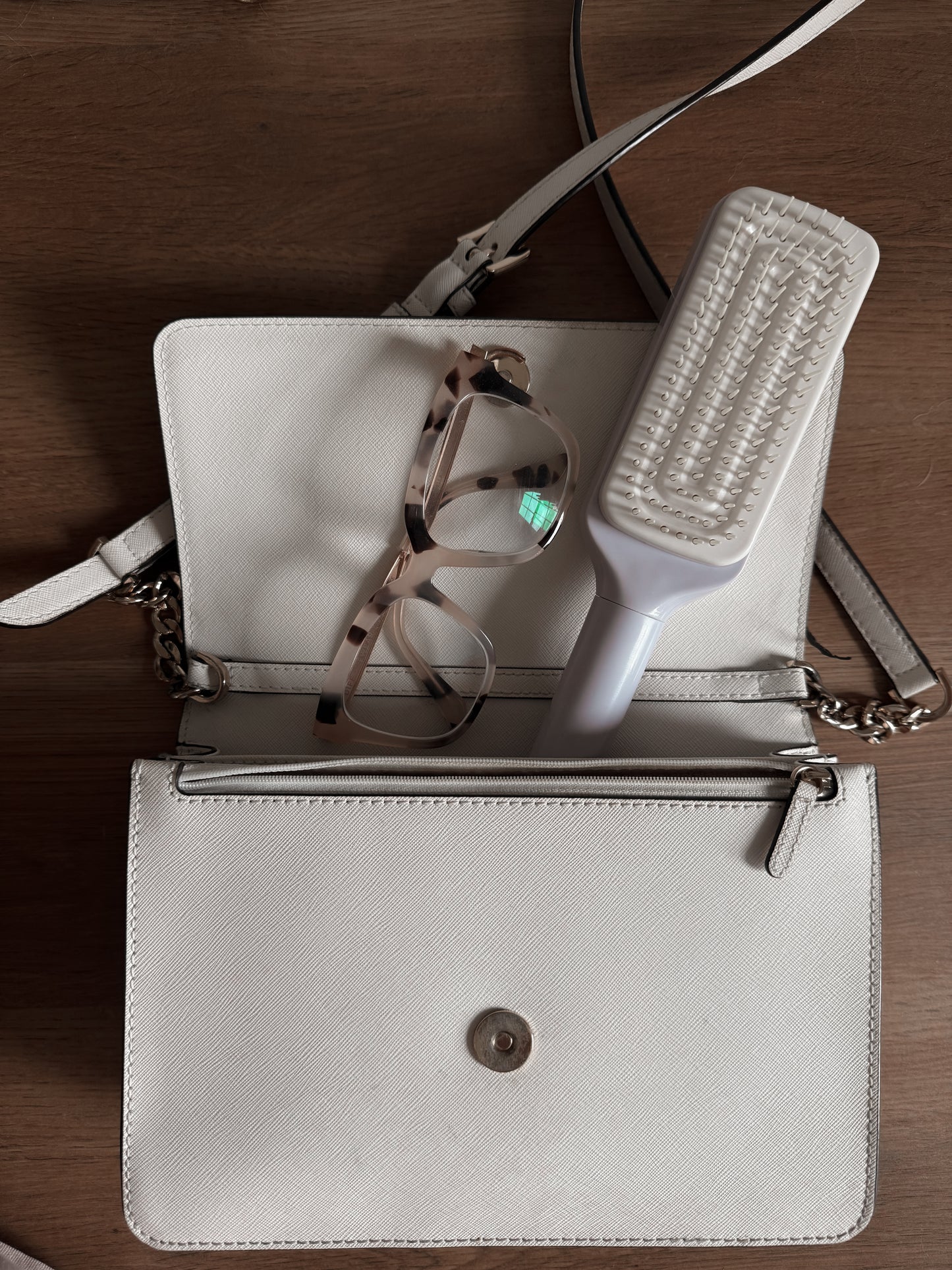 White handbag with glasses and a self cleaning hairbrush on a wooden surface